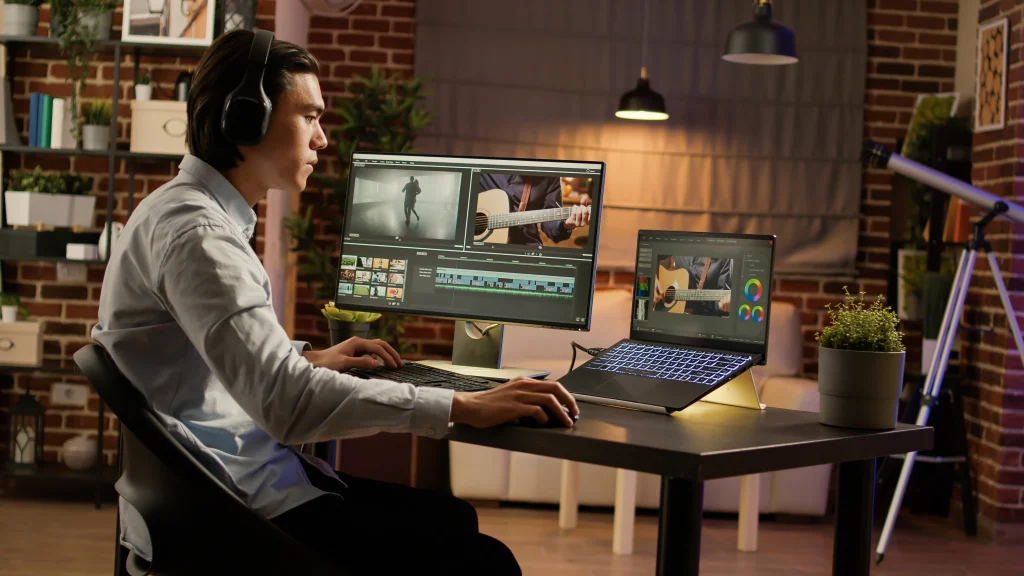 A young man with headphones using both a laptop and an external monitor to turn video into animation. The image highlights the technical setup required to convert video to animation effectively for digital projects.